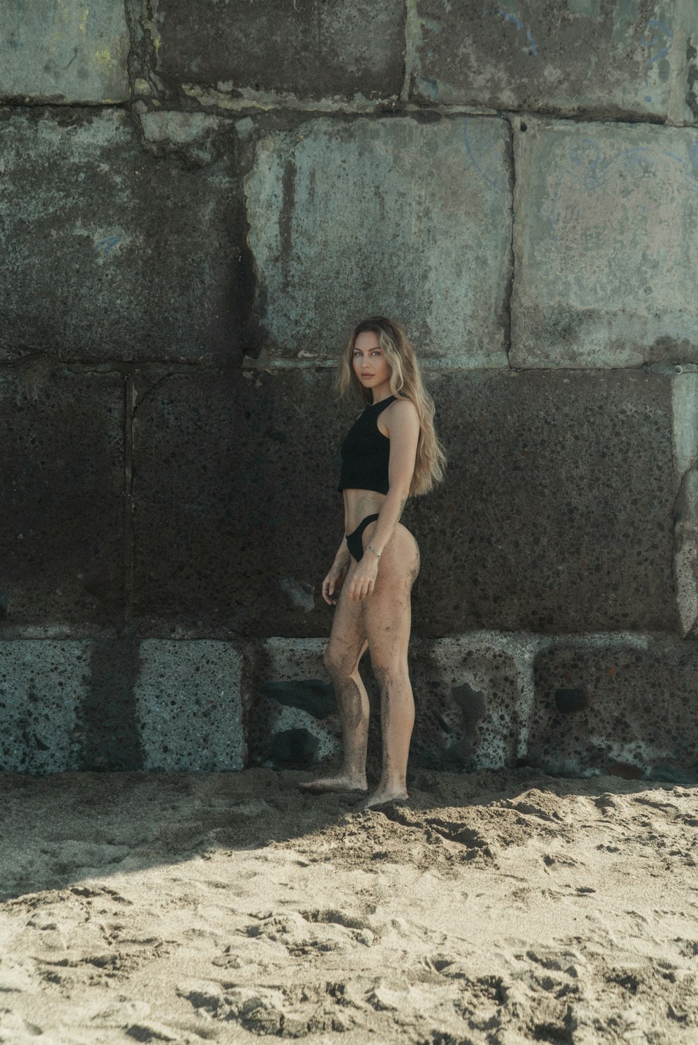 a woman in a black bikini standing in front of a stone wall