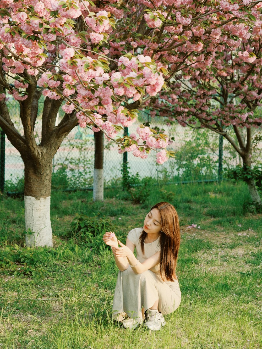 a woman sitting in the grass next to a tree