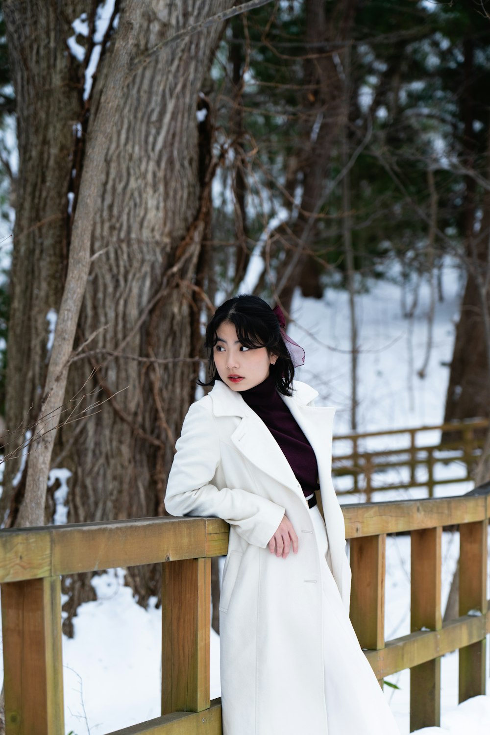 a woman in a white coat leaning on a fence