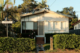 a small white house sitting next to a lush green forest