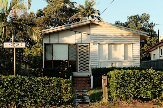 a small white house sitting next to a lush green forest