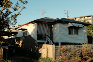 a white house with a black roof next to a fence