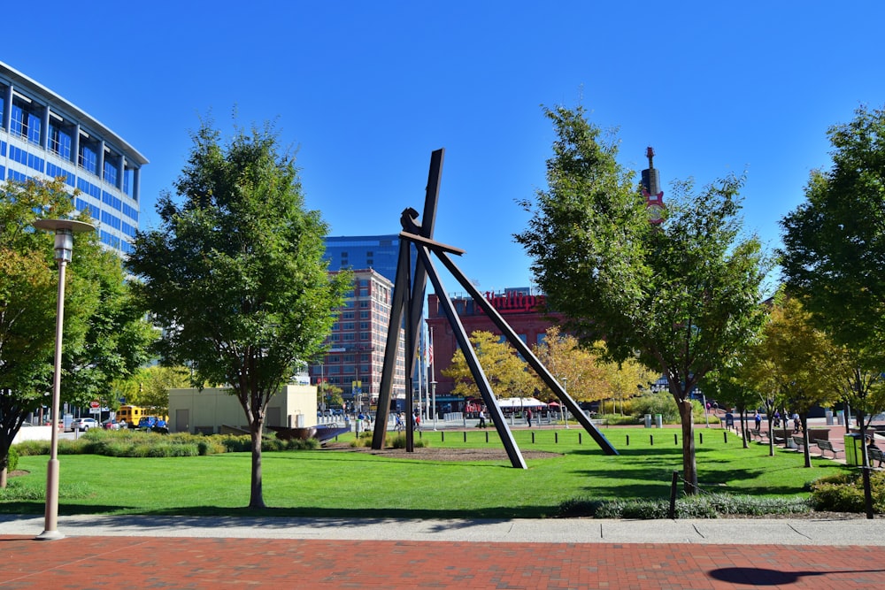 a sculpture in a park with trees and buildings in the background