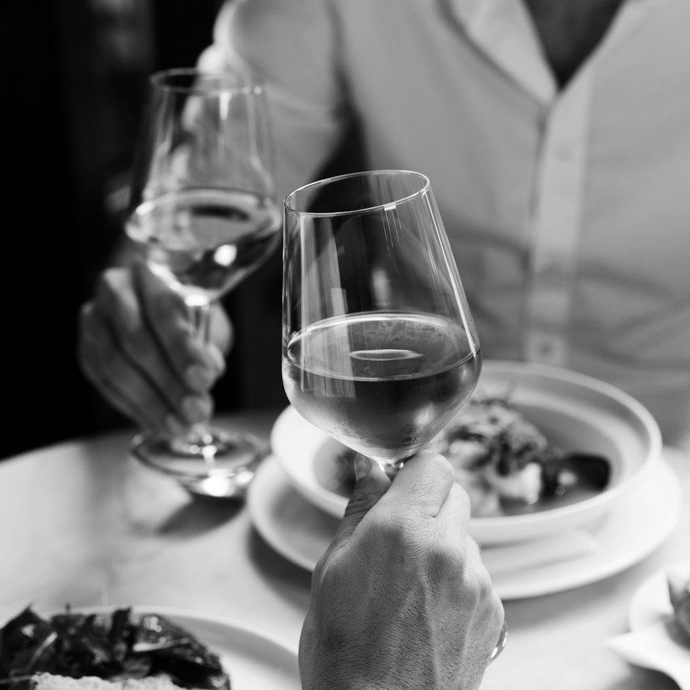 a person holding a wine glass over a plate of food