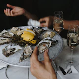 a person holding a plate of oysters with lemon wedges