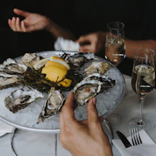 a person holding a plate of oysters with lemon wedges