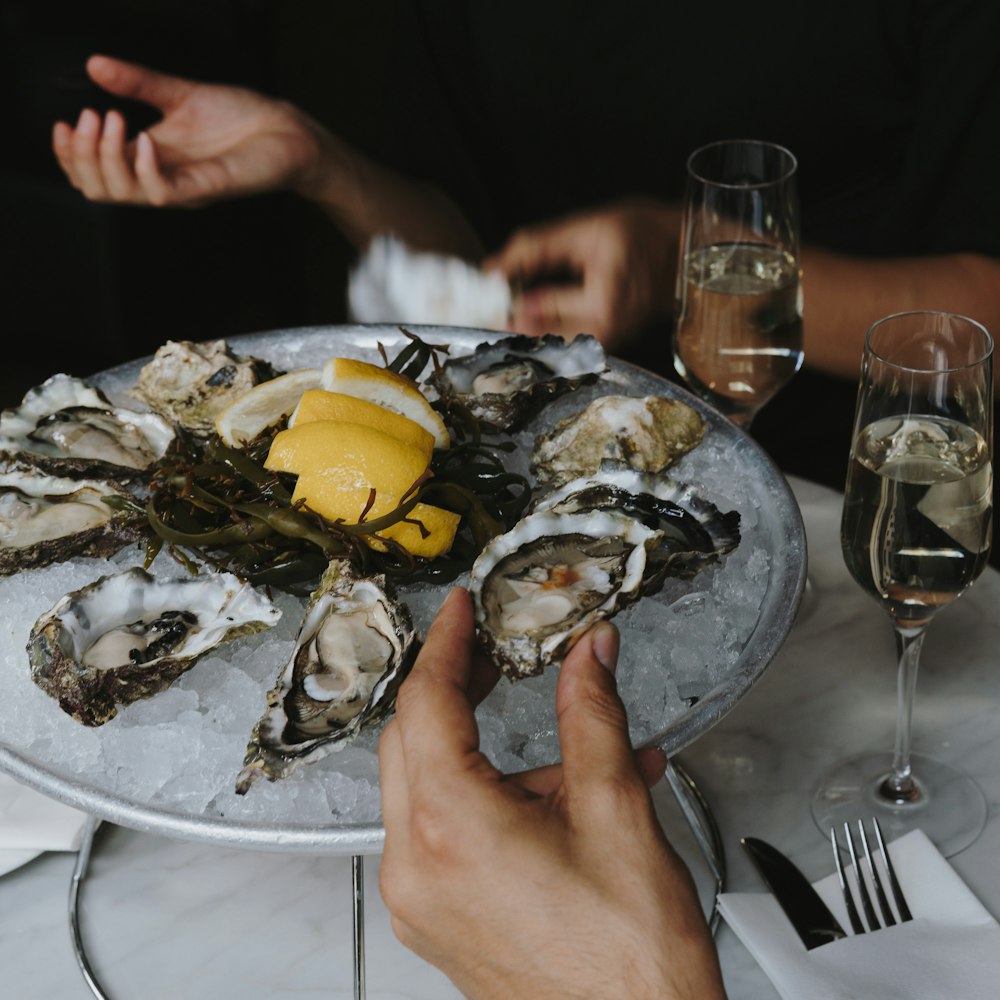 a person holding a plate of oysters with lemon wedges