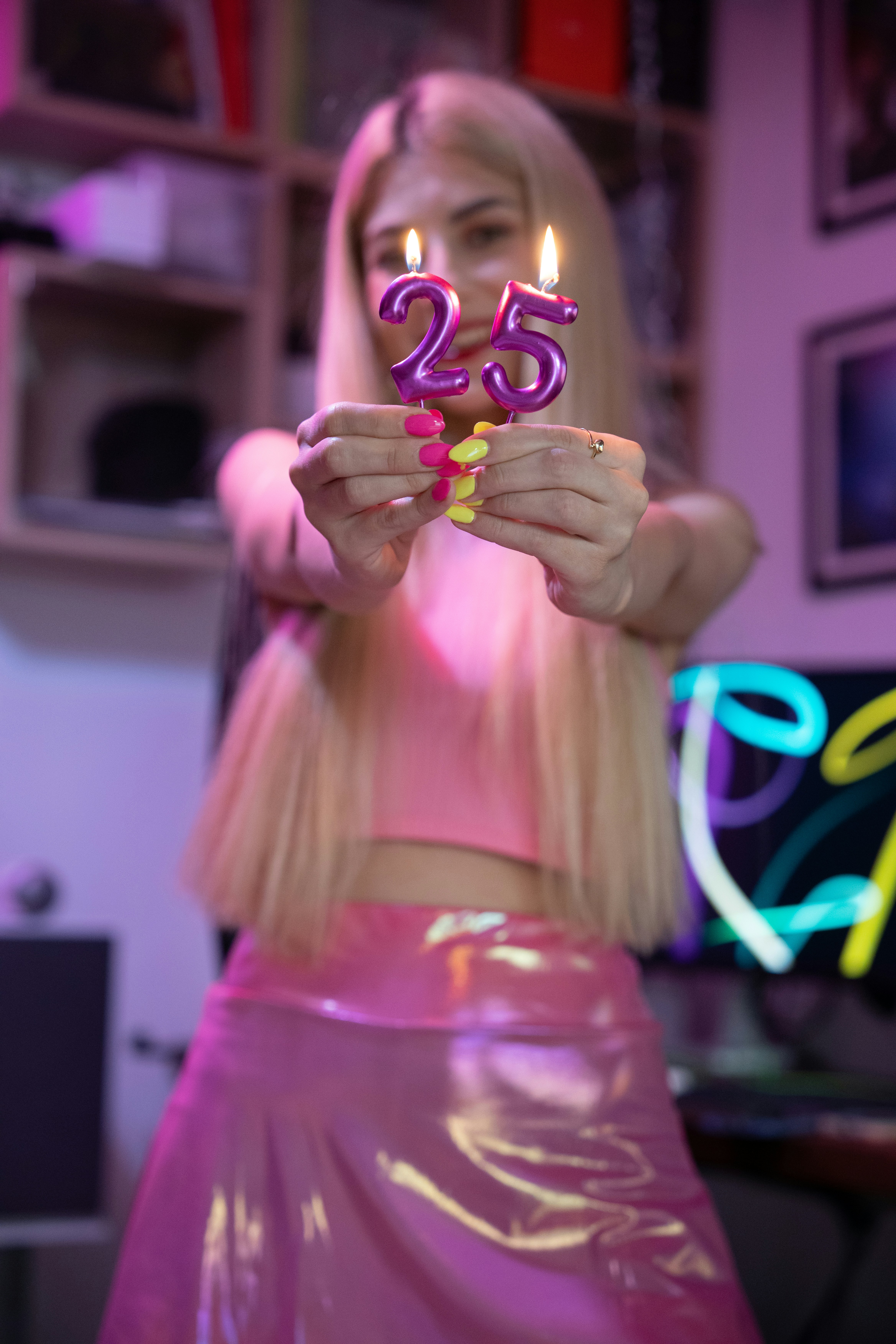 A beautiful blonde young woman dressed in pink celebrates her birthday by holding candles showing her age