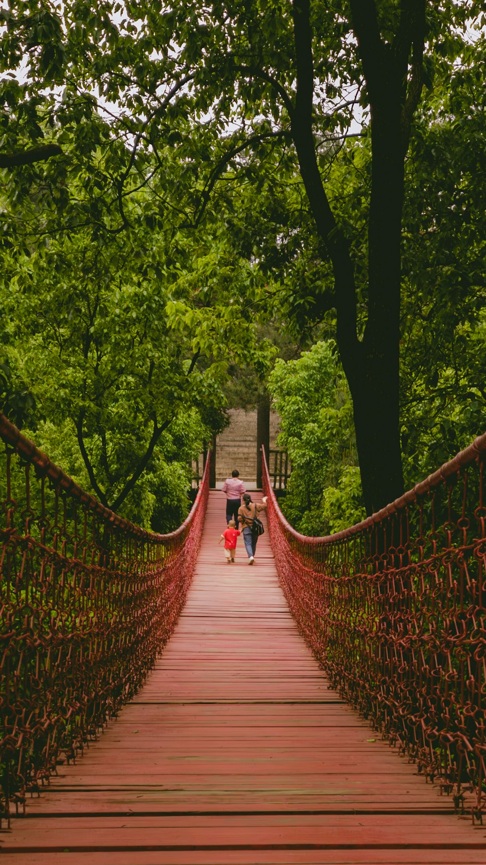 two people walking across a red bridge in the woods