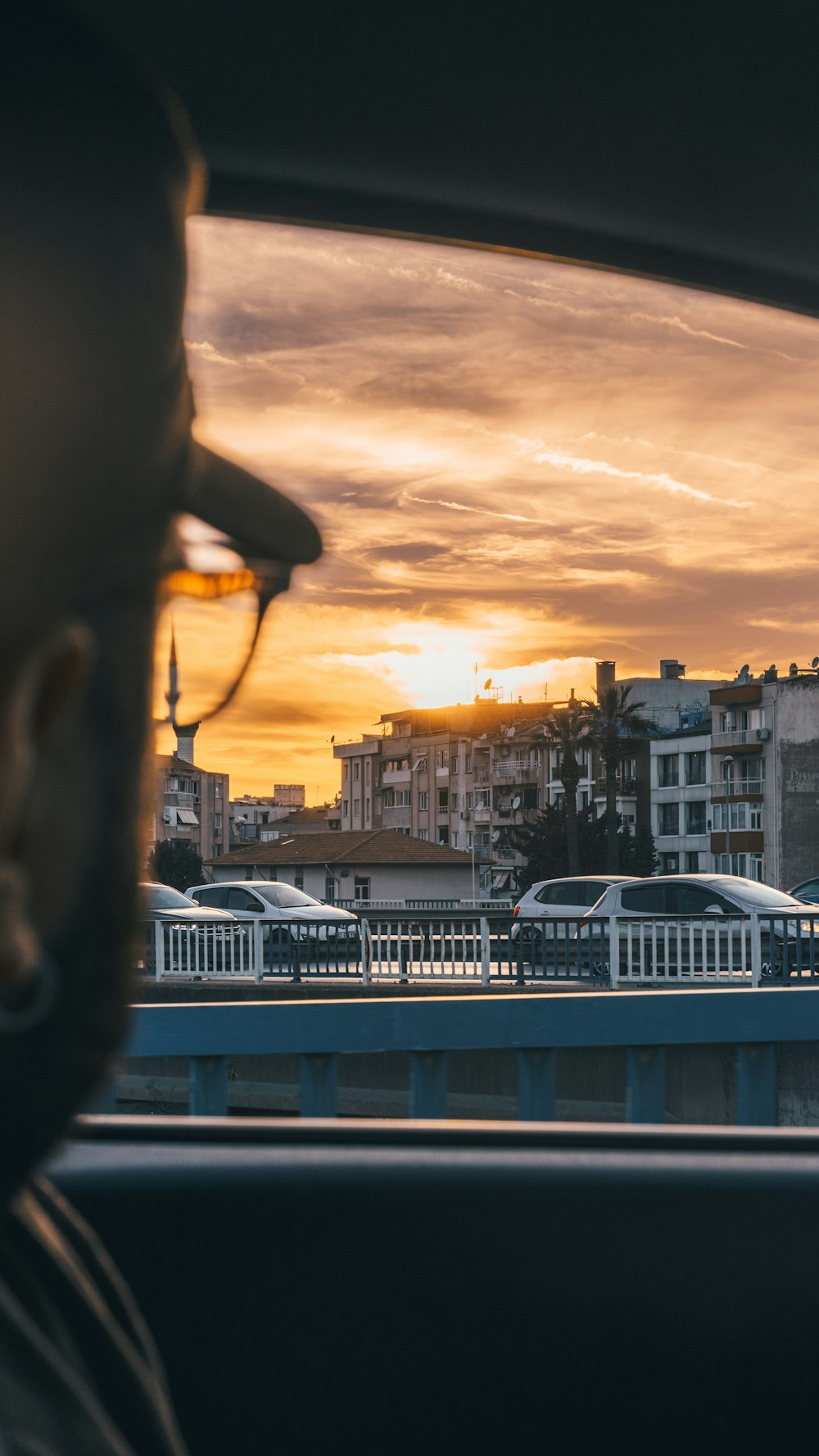 a man in a car looking out the window at a sunset