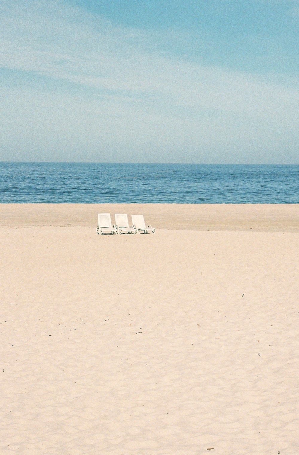 a couple of lawn chairs sitting on top of a sandy beach