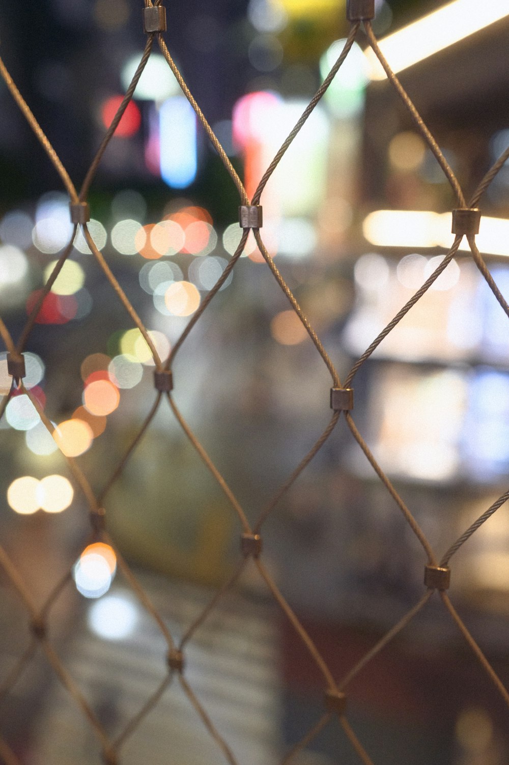 a close up of a chain link fence with blurry lights in the background