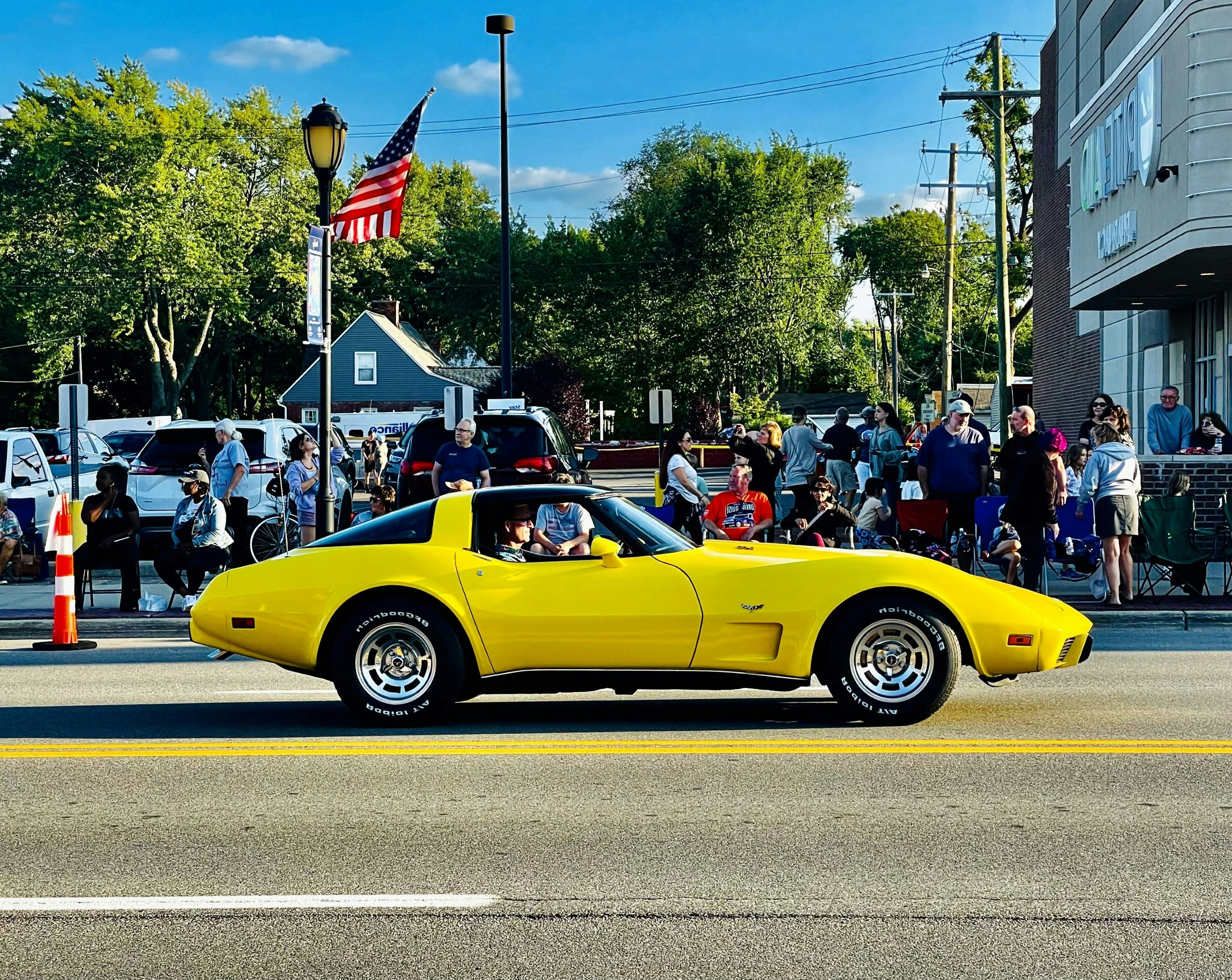 a yellow car driving down a street past a crowd of people