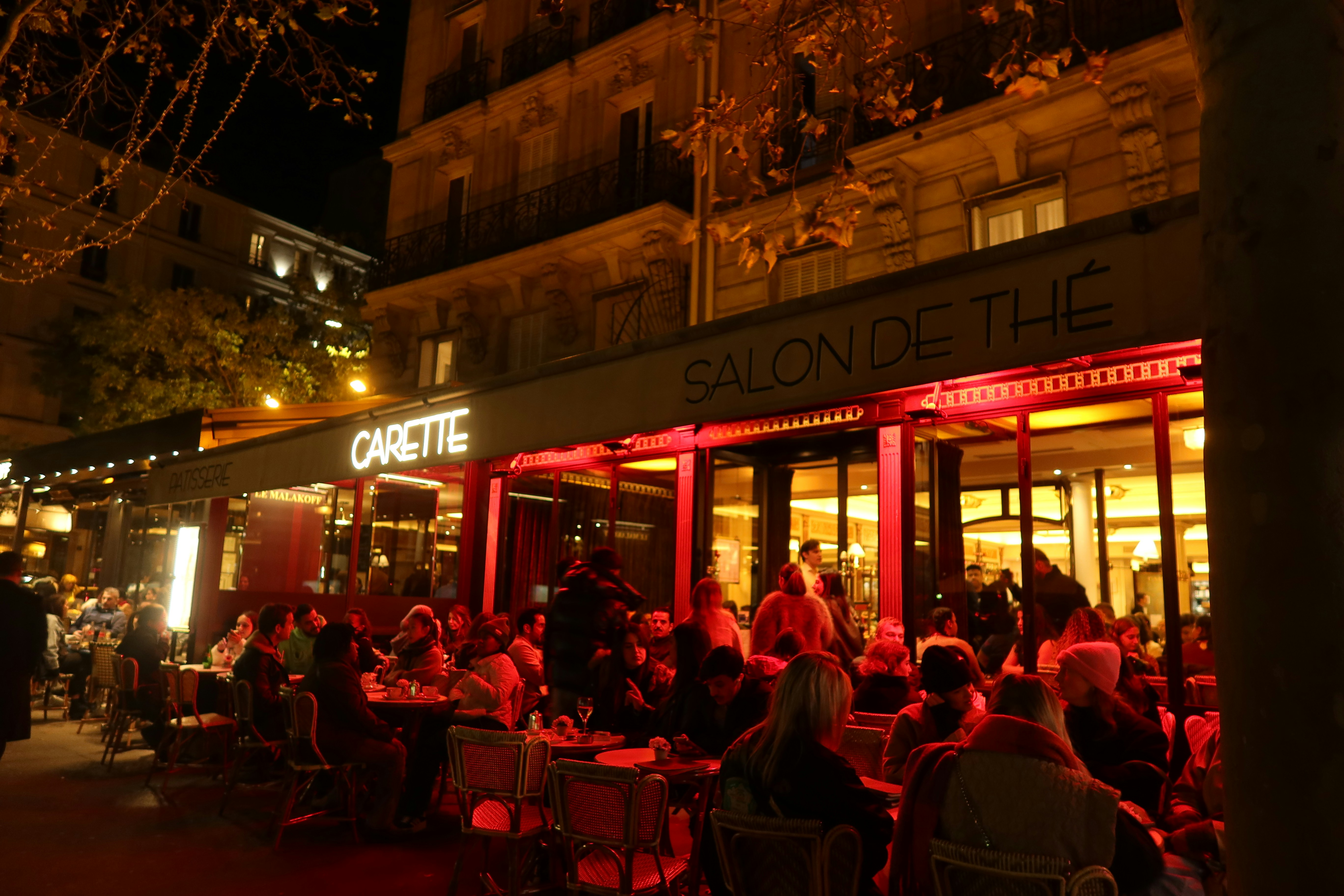 a group of people sitting outside of a restaurant at night