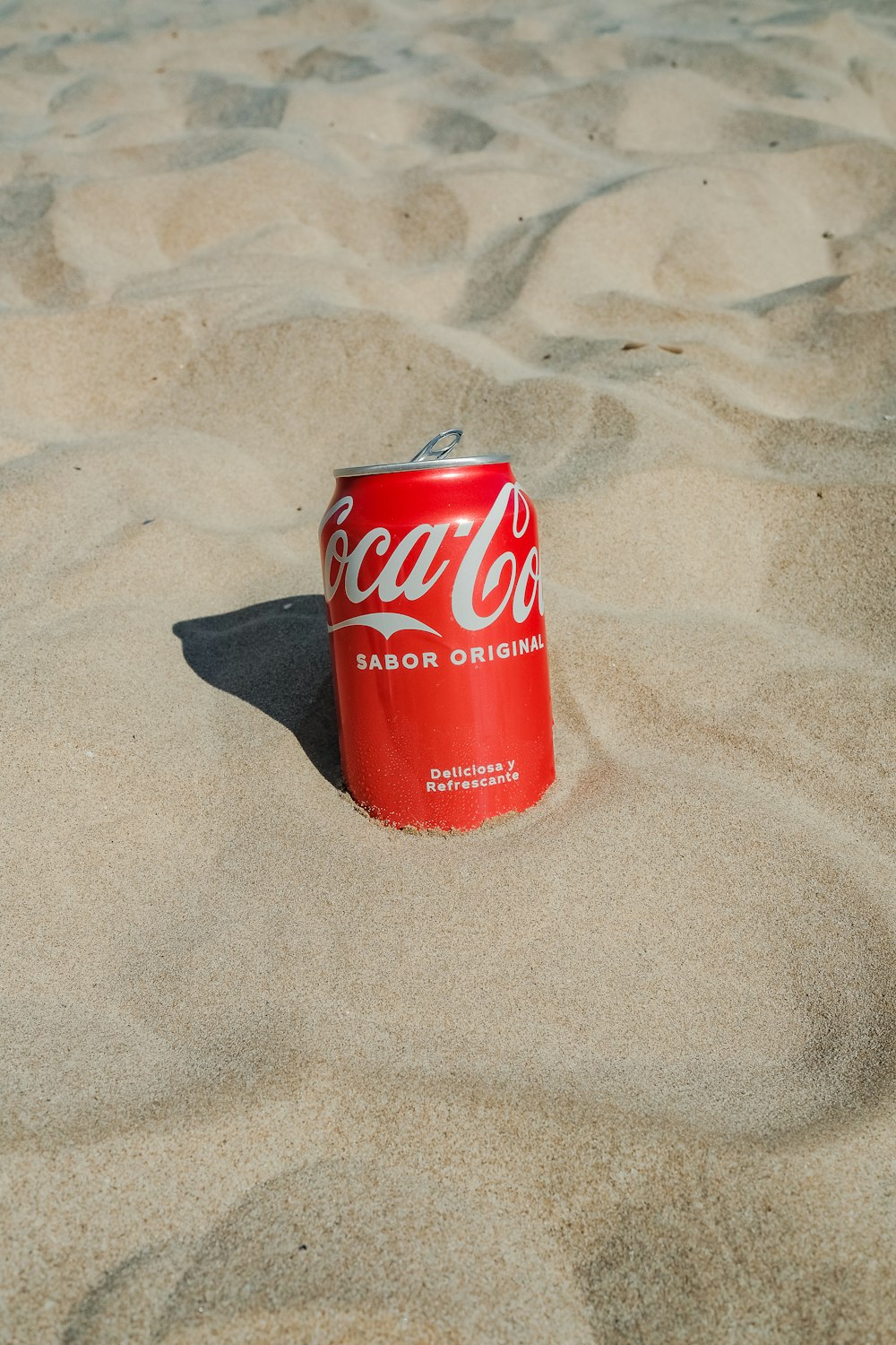 a can of coca cola sitting in the sand
