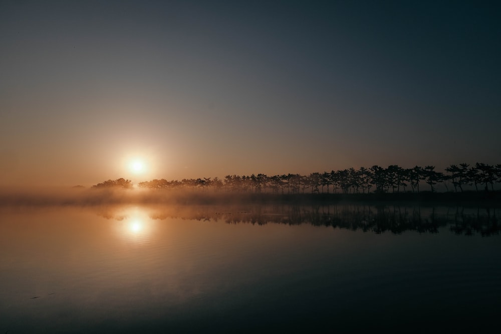 the sun is setting over a calm lake