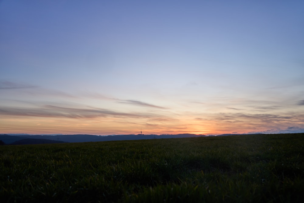 the sun is setting over a grassy field