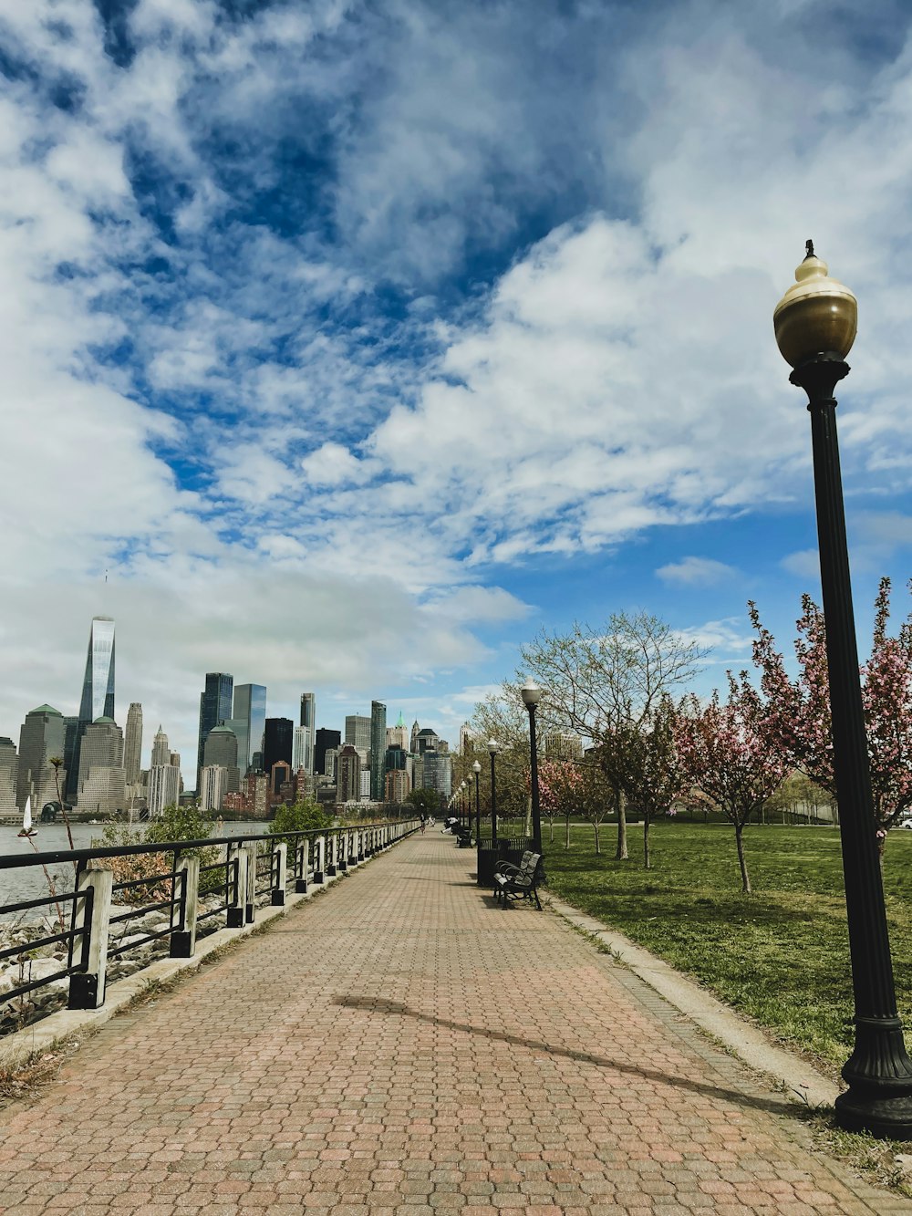 a brick walkway leading to a park with a city in the background