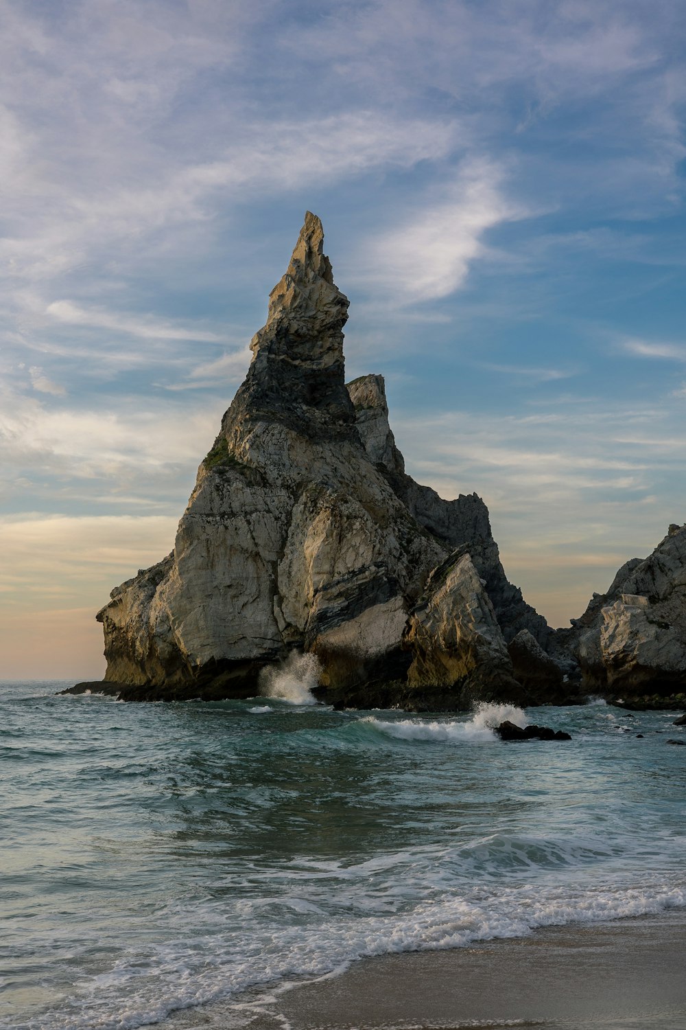 una grande roccia che spunta dall'oceano vicino a una spiaggia
