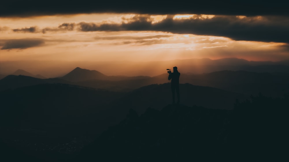 une personne debout au sommet d’une montagne au coucher du soleil