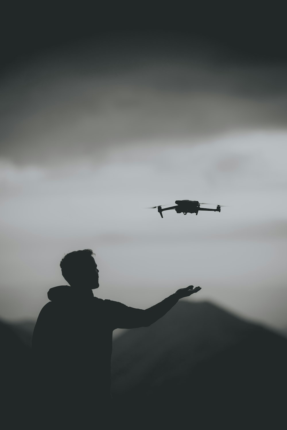 a black and white photo of a man with a remote control plane in the sky