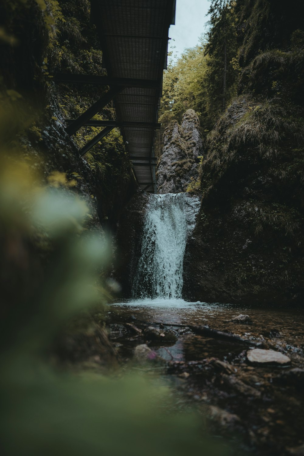 a small waterfall under a bridge in the woods