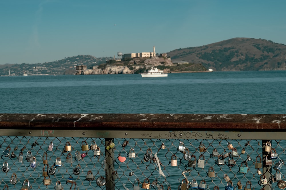 a chain link fence covered in padlocks with a boat in the background