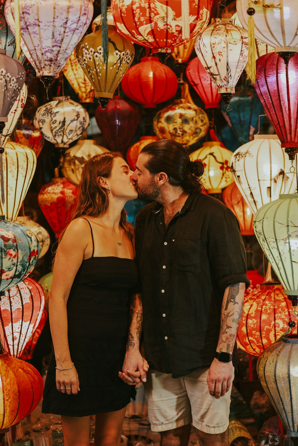 a man and a woman kissing in front of a wall of lanterns