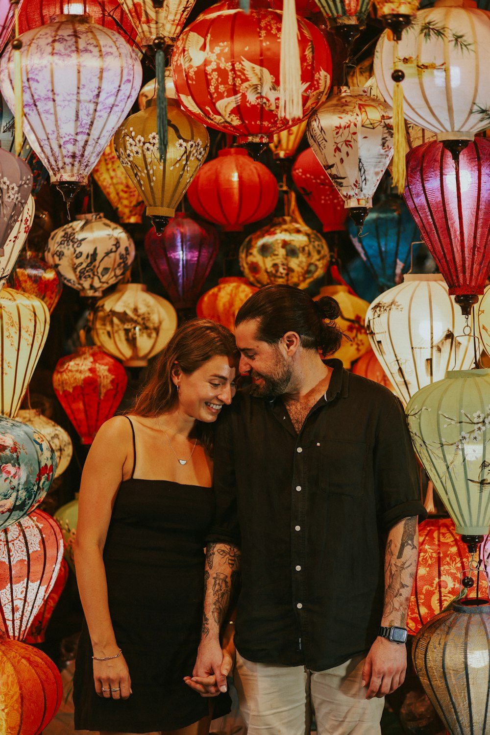 a man and a woman standing in front of a wall of lanterns