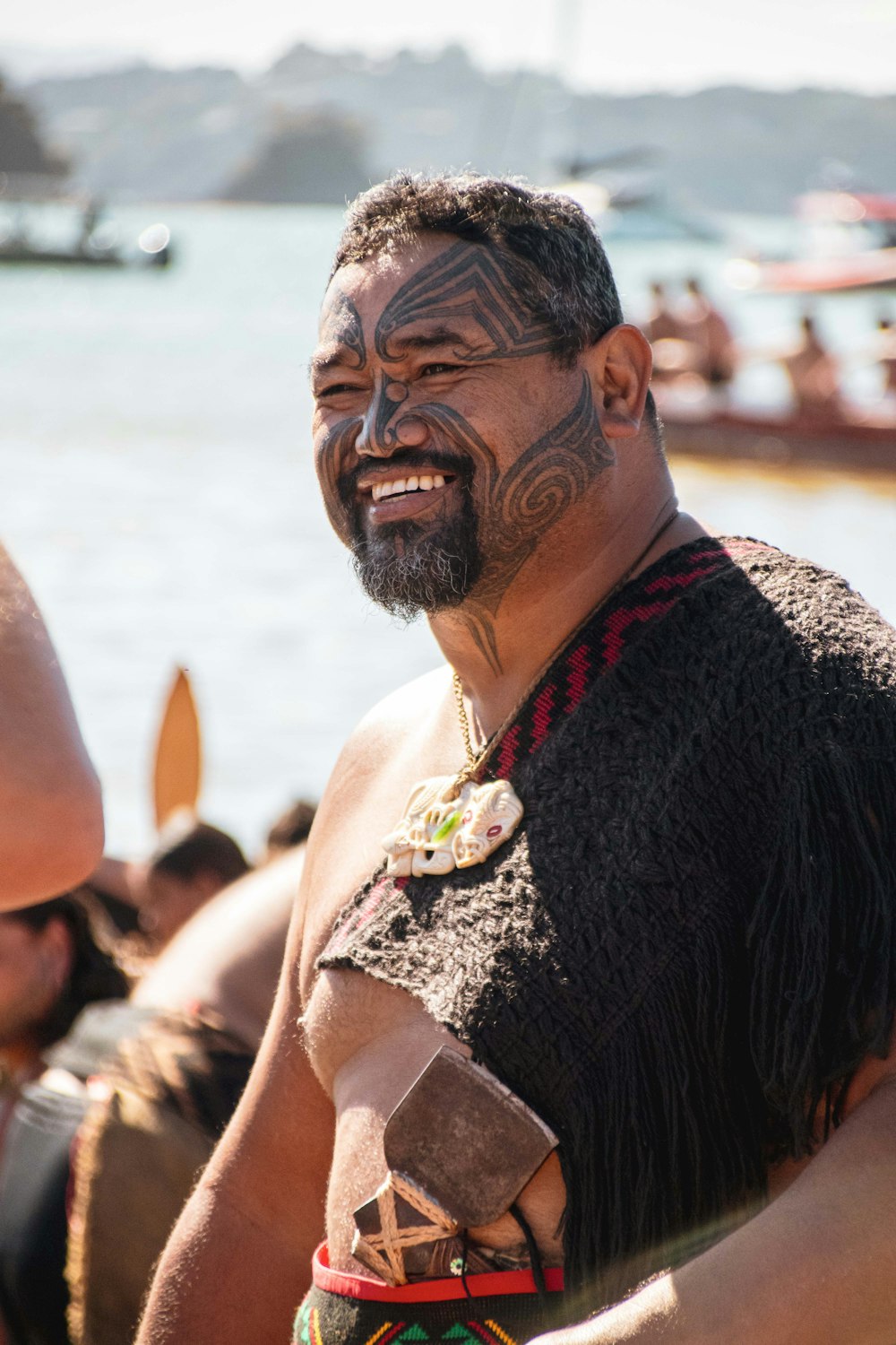 a man with a beard and tattoos standing next to a body of water