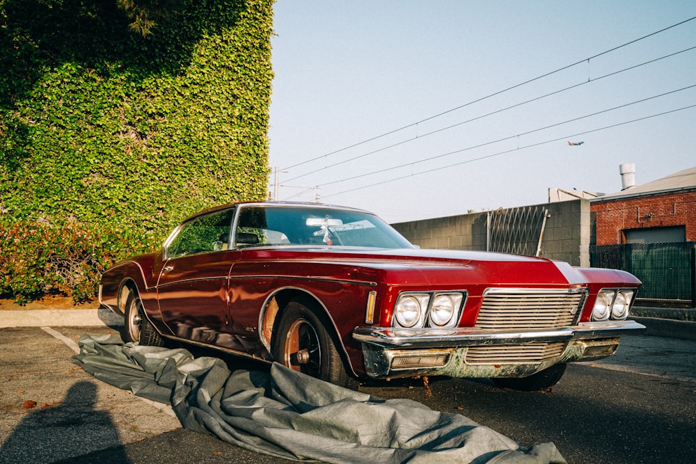 a red car parked in front of a green hedge