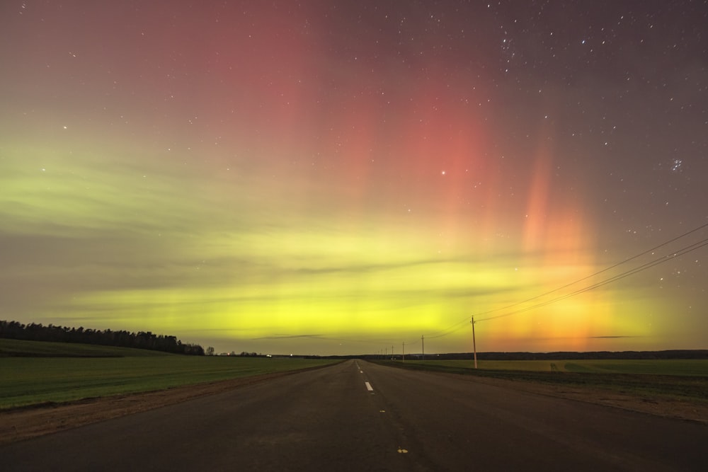 a road with a green and red aurora light in the sky