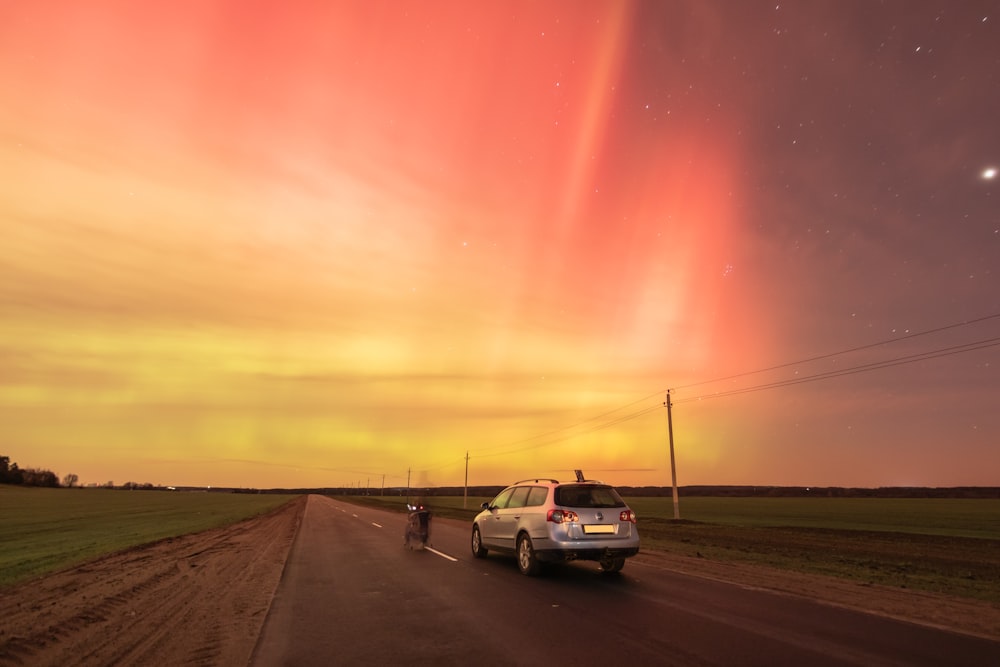 a car driving down a road under a colorful sky