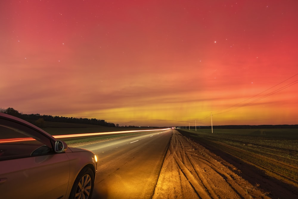 a car driving down a road under a red sky