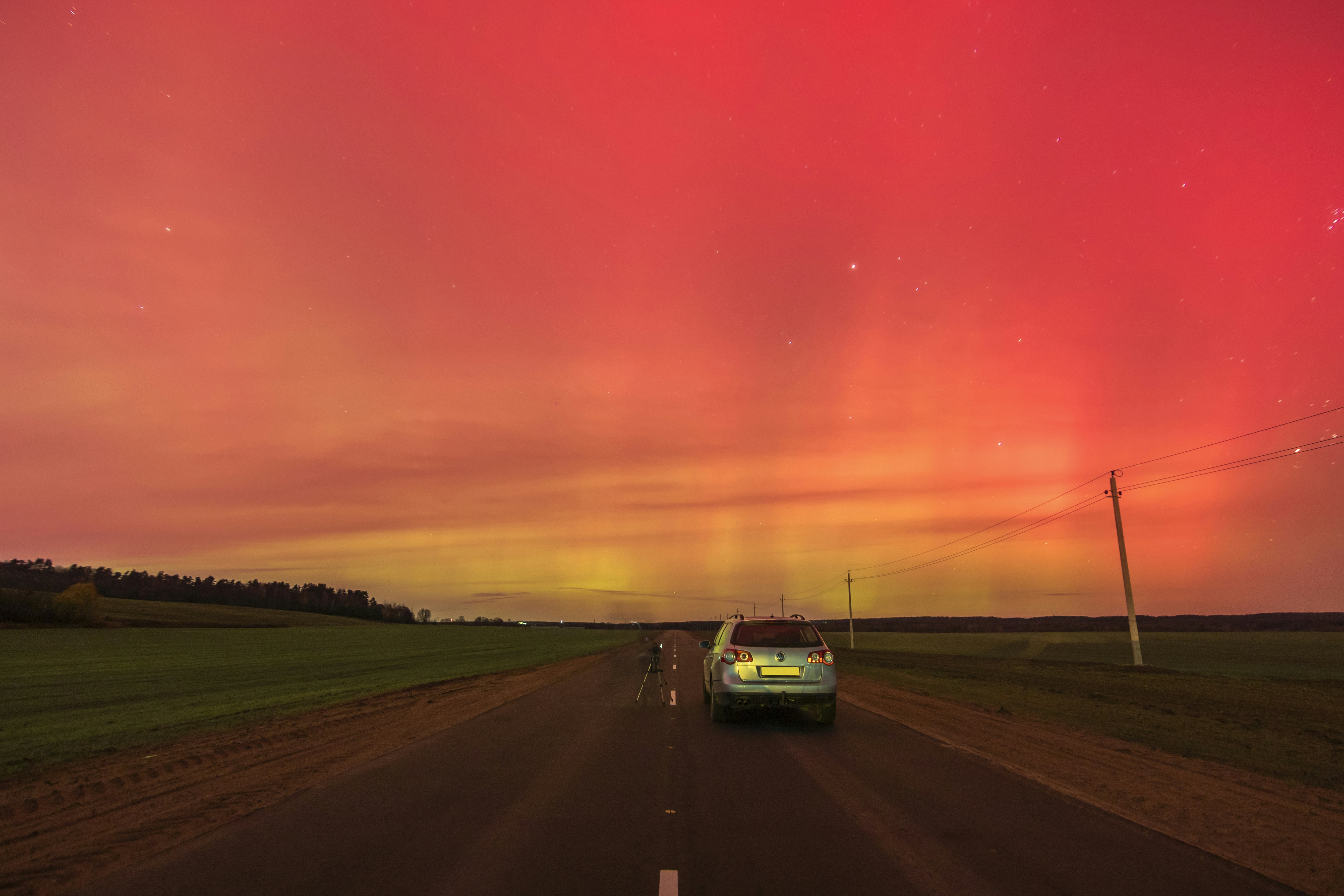 a car driving down a road under a red sky