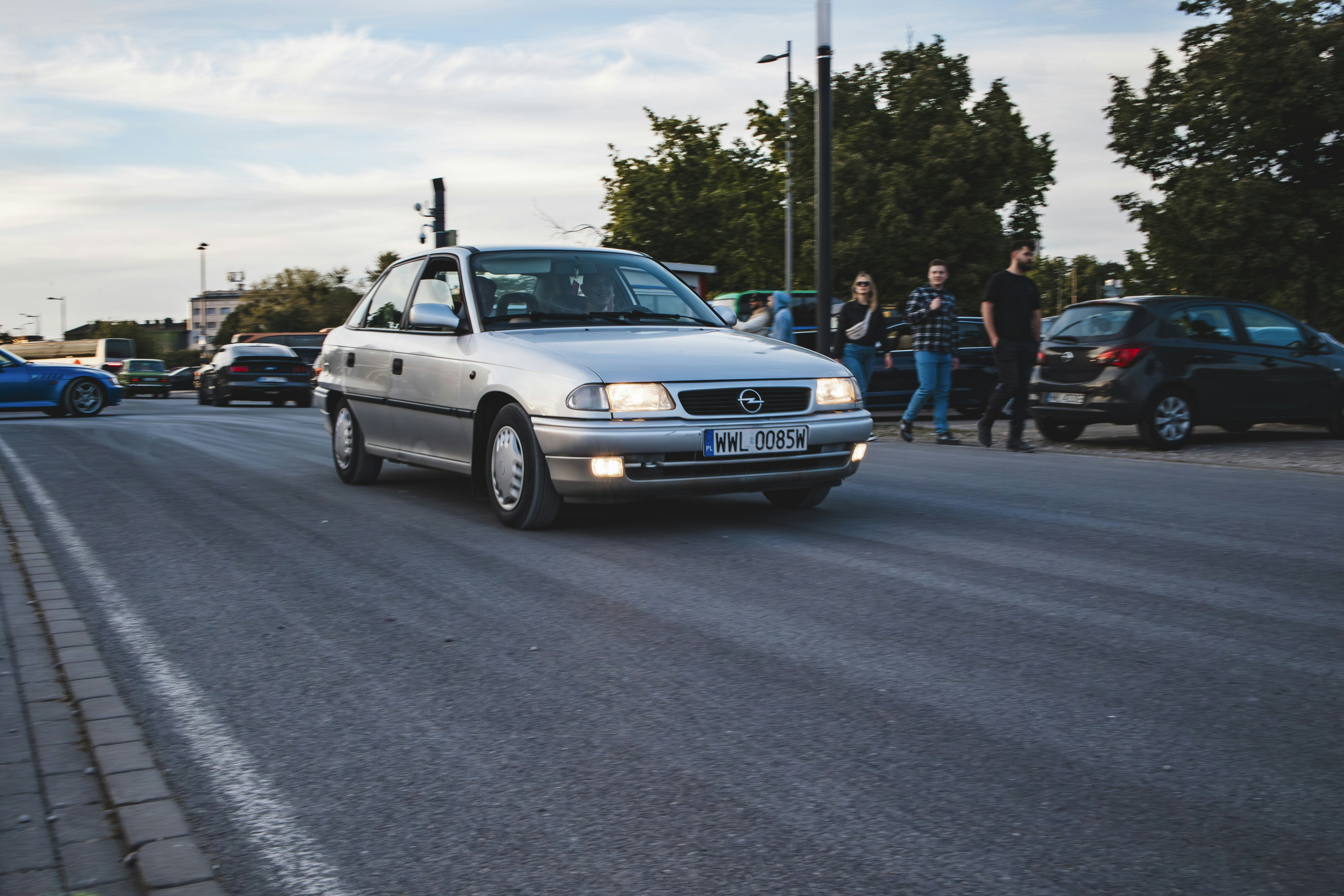 a white car driving down a street next to parked cars