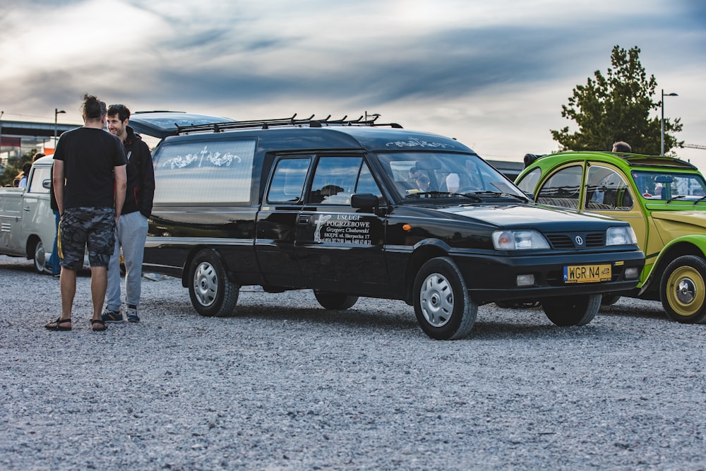 a couple of men standing next to a parked car