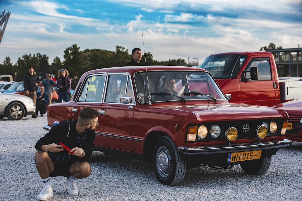 a man kneeling down next to a red car