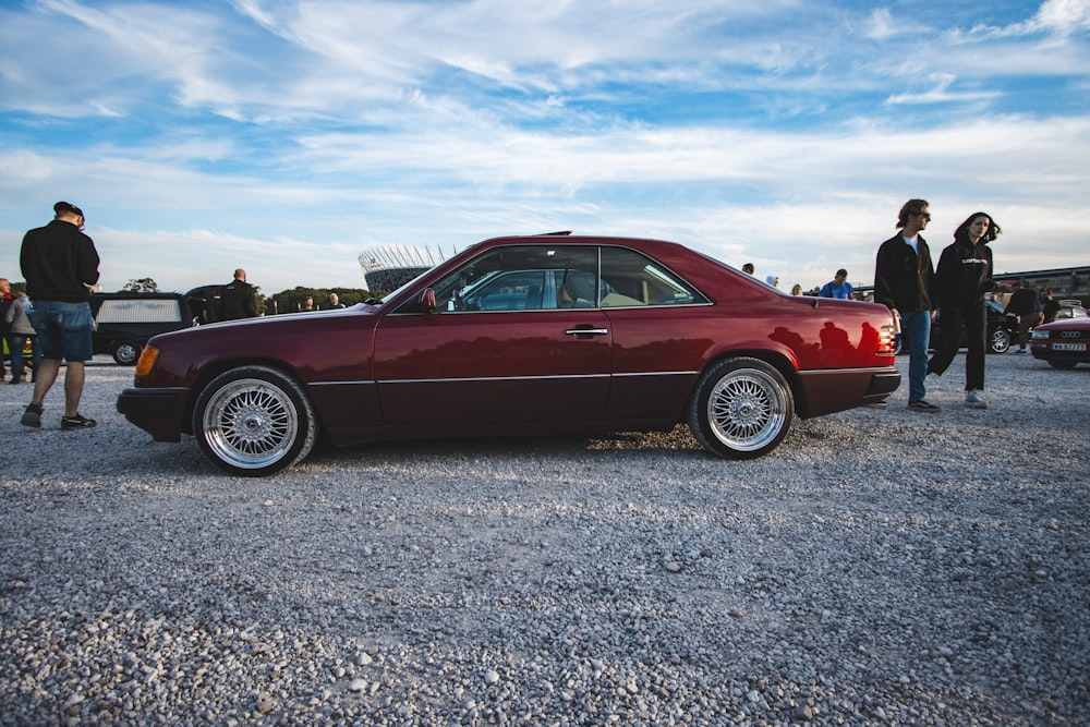 a maroon car is parked in a gravel lot