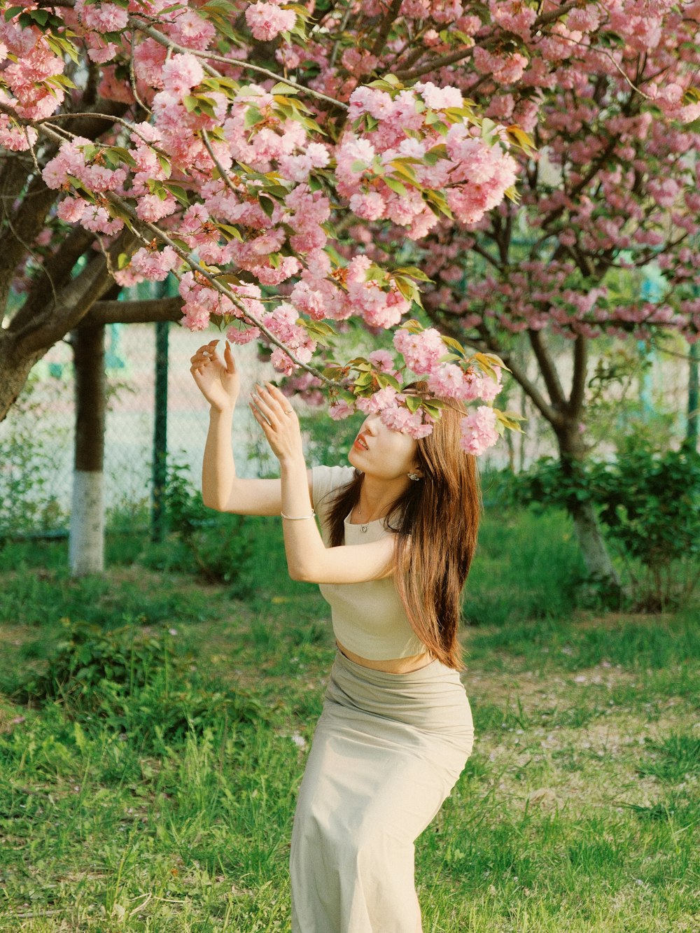 a woman is standing under a tree with pink flowers