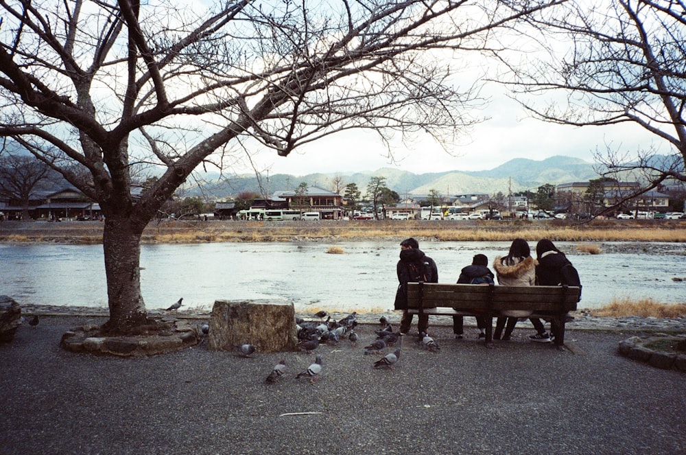 a group of people sitting on a bench next to a river