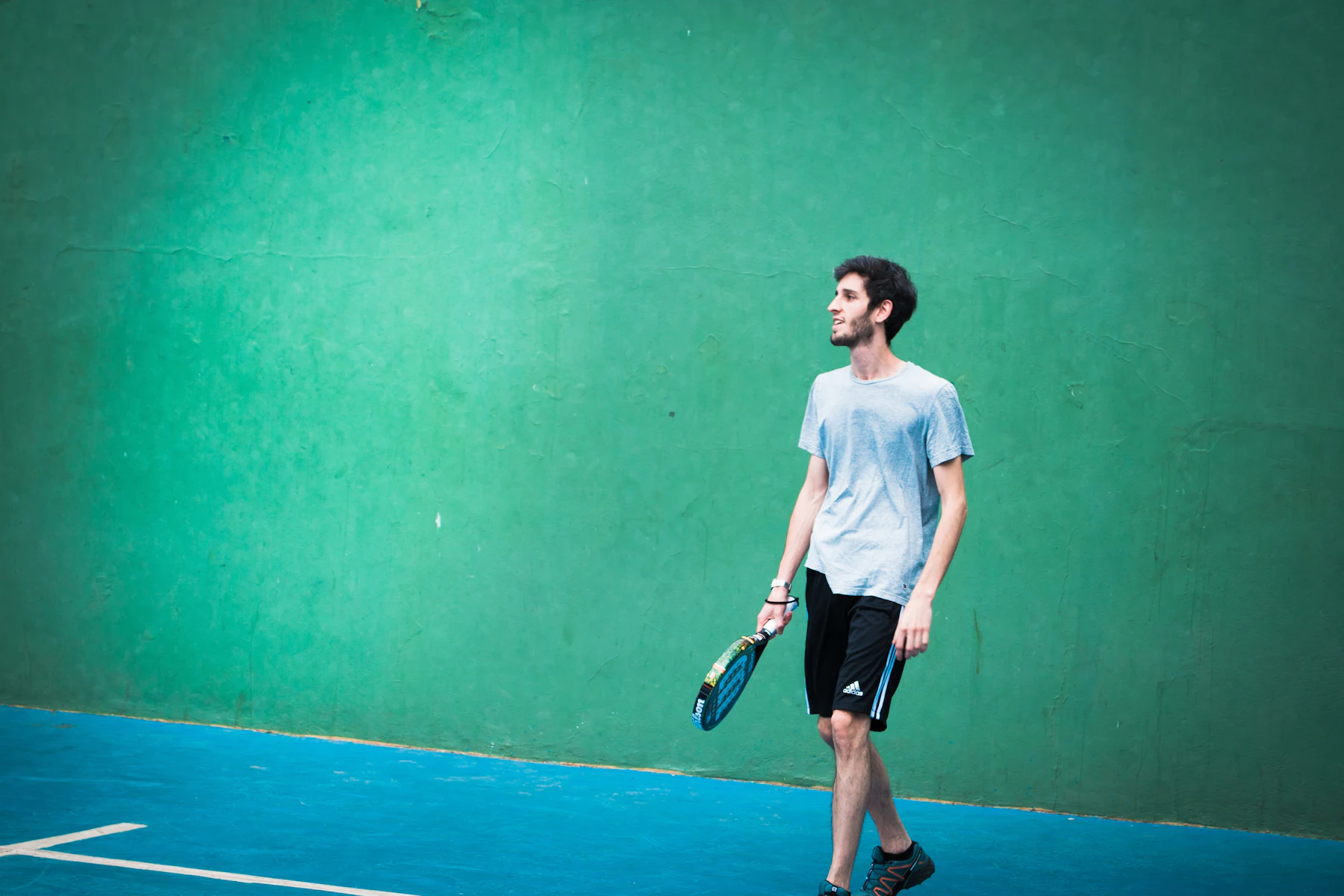A padel player walks back into position on a court with a high green wall