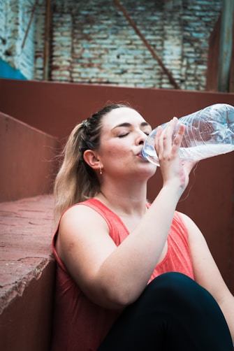 a woman drinking water from a plastic bottle