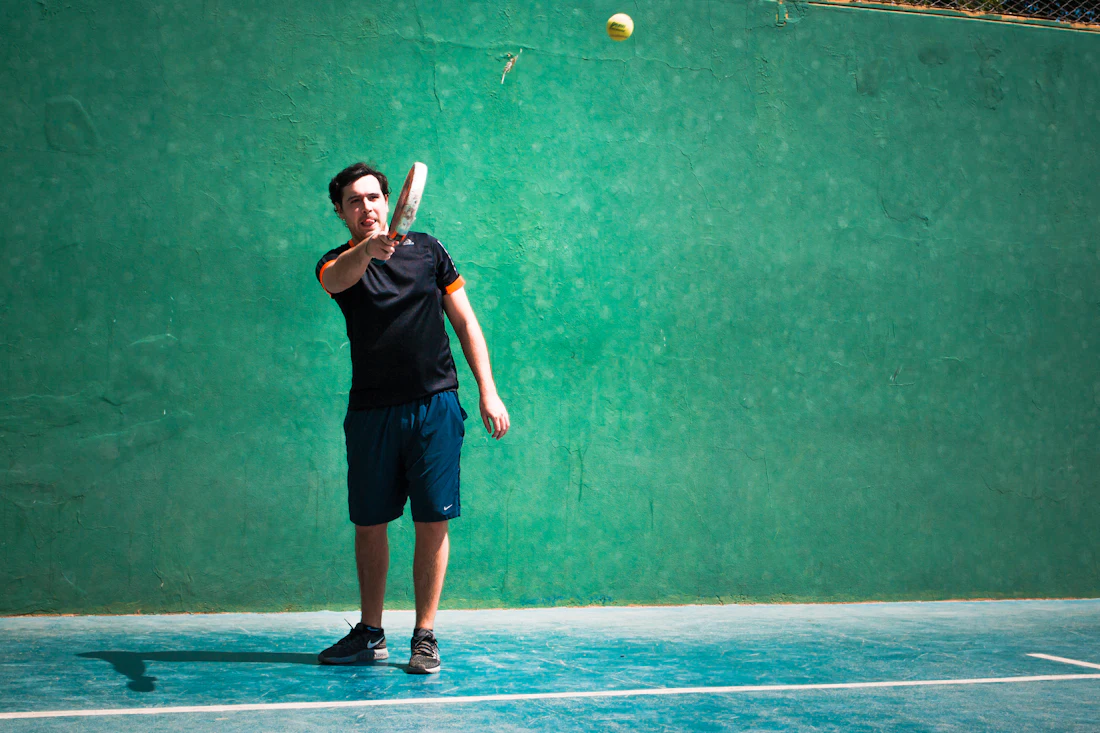 A padel player hits a forehand in front of a green court wall