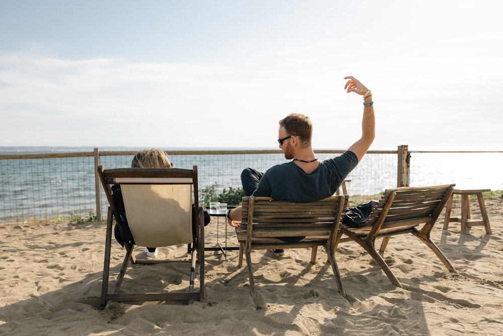 a man sitting on top of a wooden chair on top of a sandy beach