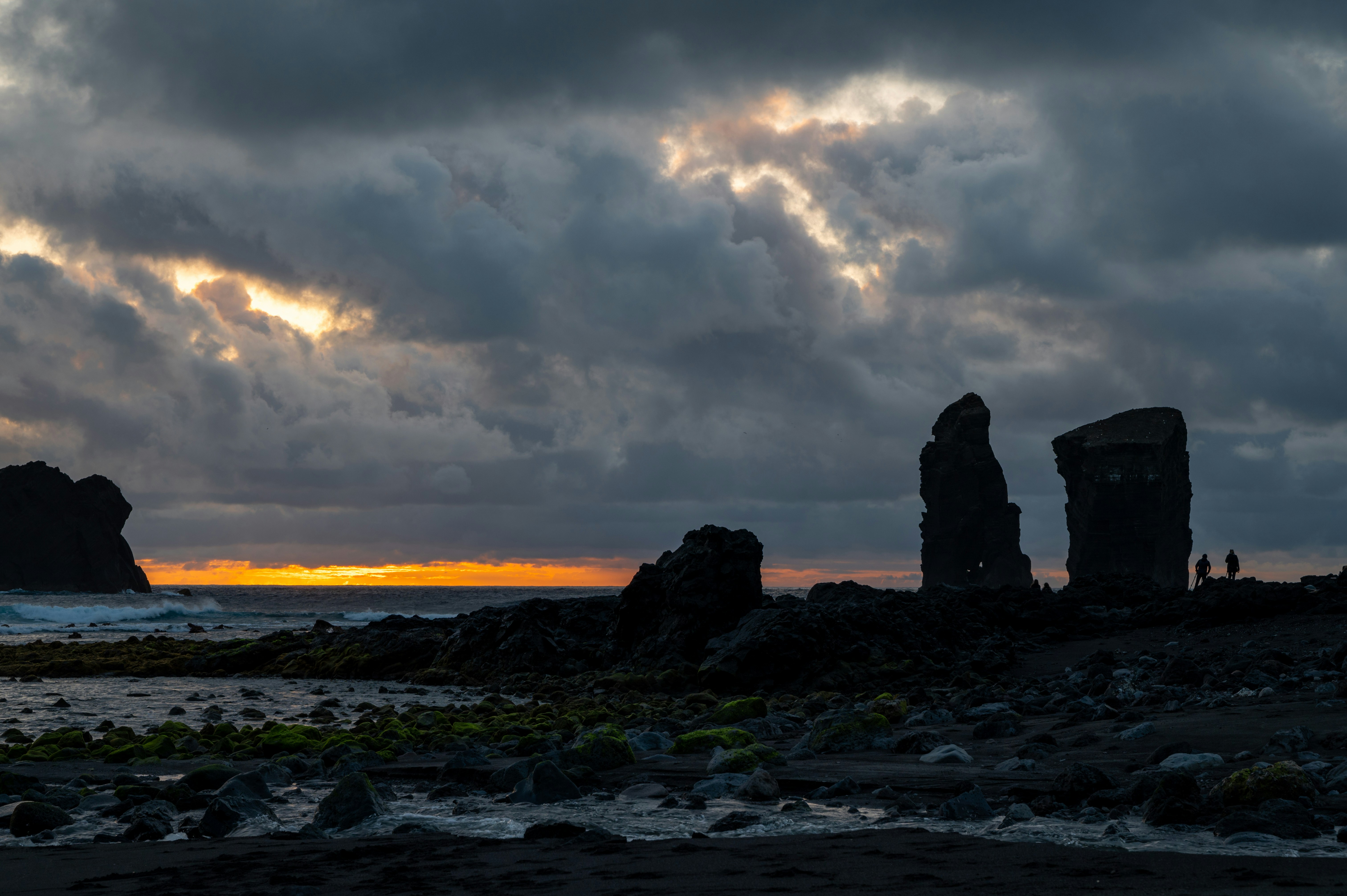 a group of rocks sitting on top of a beach under a cloudy sky