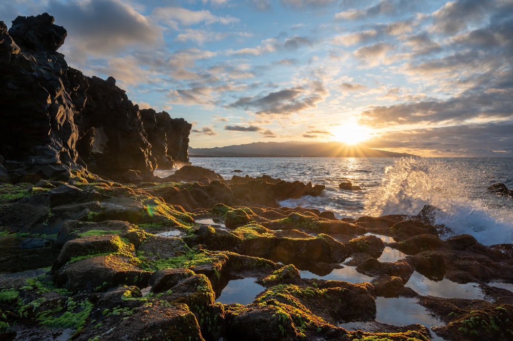 the sun is setting over a rocky shoreline
