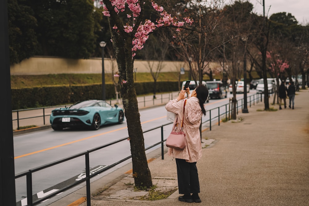 a woman standing on a sidewalk next to a tree