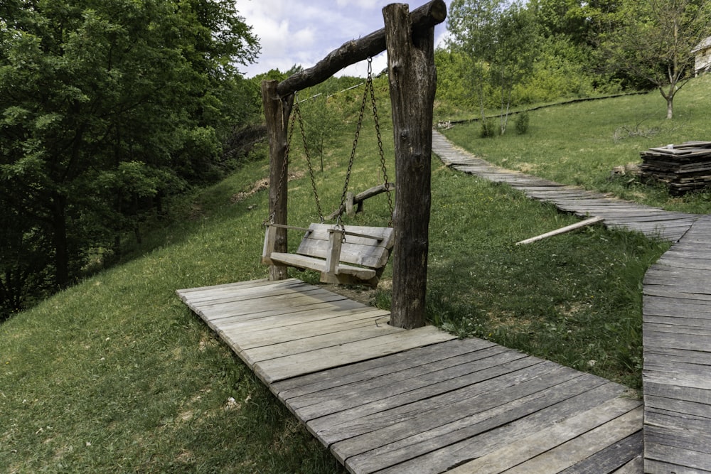 a wooden swing sitting on top of a lush green hillside