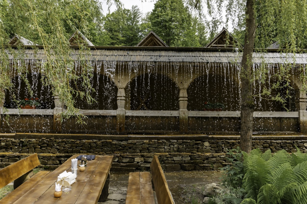 a wooden table sitting under a waterfall next to a forest